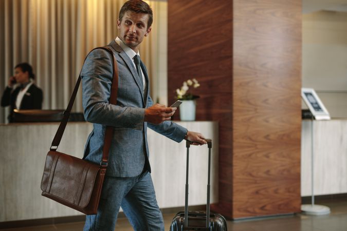 Businessman in hotel hallway with phone and baggage