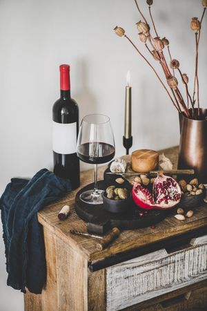 Rustic setting of wine, cheese, long candle, with pomegranate, and dried poppies