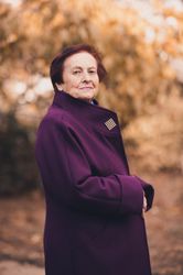 Side view of older woman in purple coat standing near yellow trees