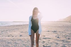 Young woman standing on beach with sunset at her back
