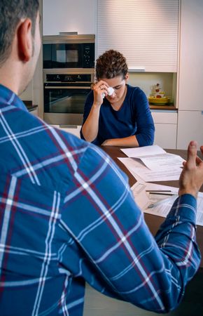 Woman holding tissue to face as her and her partner argue over bills