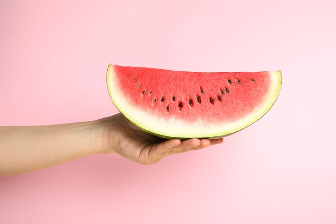 Female hand holds watermelon slice on pink background. Summer fruit
