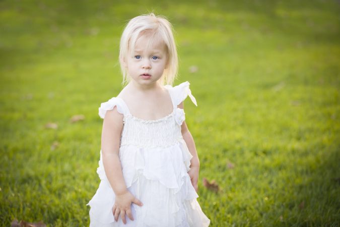 Adorable Little Girl Wearing White Dress In A Grass Field