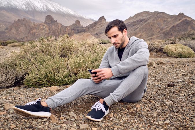 Content male reading message on smartphone sitting on rocky terr