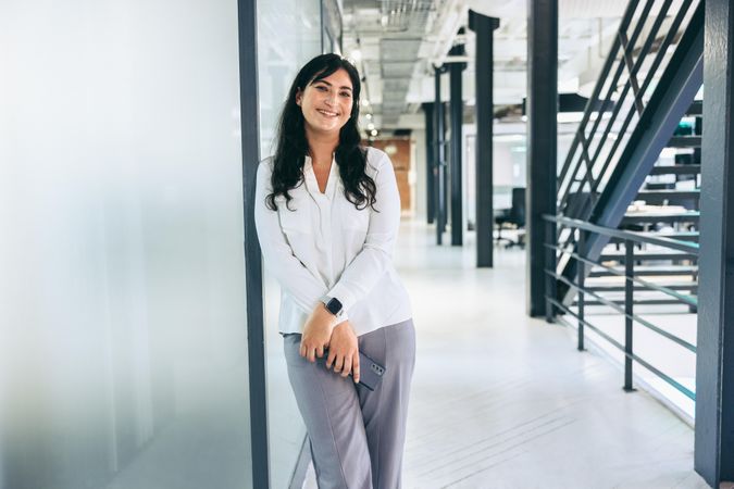 Happy businesswoman smiling at the camera in bright office with metal stairs