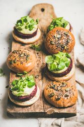 Fresh vegan burgers on seeded buns arranged on wooden bread board