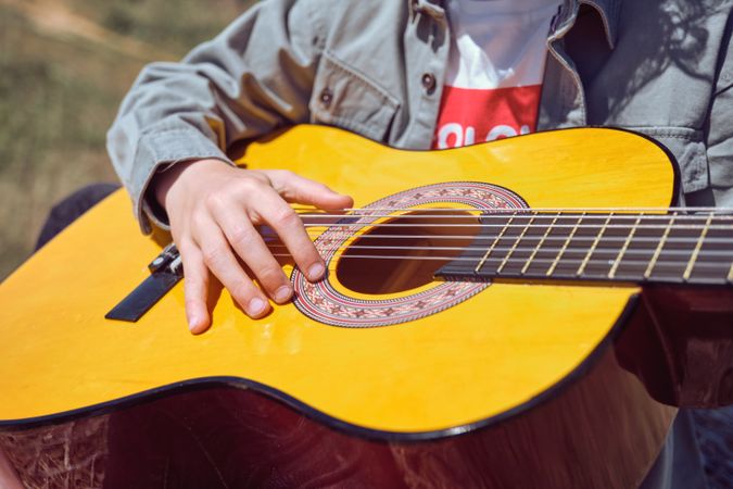 Crop unrecognizable child playing guitar in nature