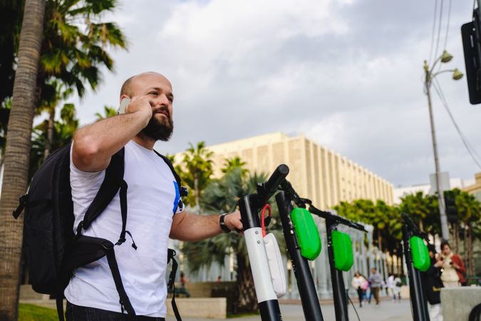 Traveler with backpack browsing smartphone and choosing electronic scooter