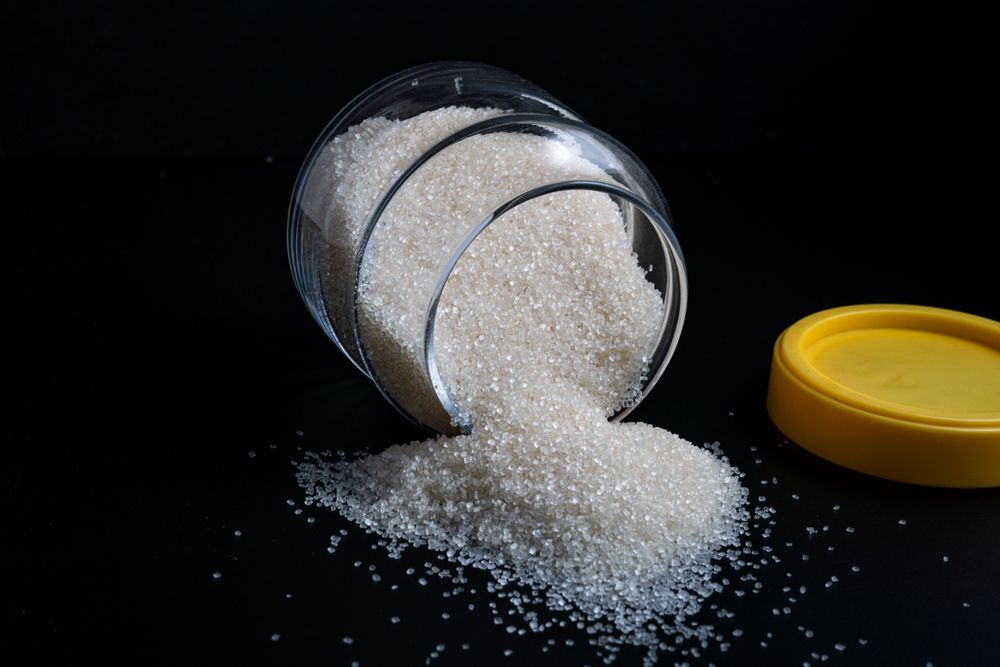 granulated sugar spilling from a glass jar onto a dark surface