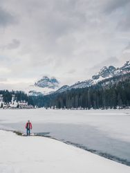 Unrecognizable person standing in snow surrounded by forest and mountains