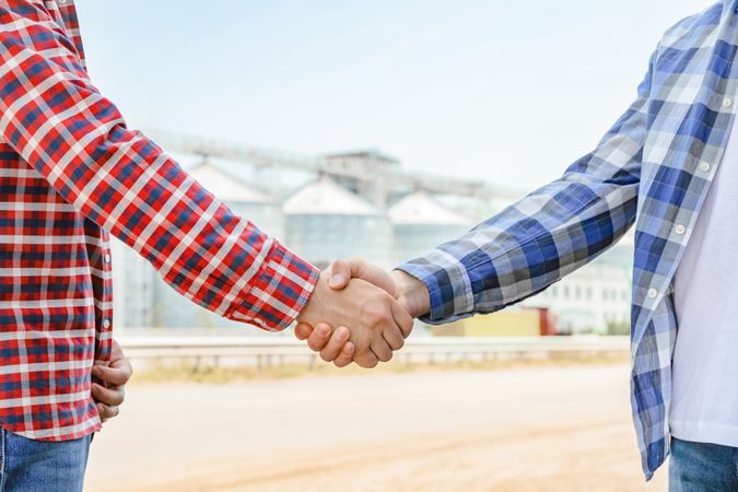 Businessmen shake hands against silos. Agriculture business