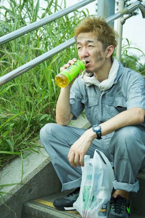 Man in work suit sitting on staircase holding a green bottle