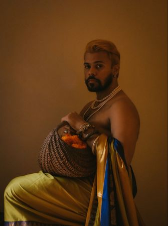 Topless man holding a wicker basket sitting on a chair against yellow background