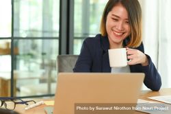 Smiling business woman drinking coffee during online meeting bYBwY0