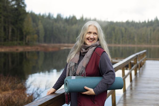 Smiling  woman holding yoga mat on dock