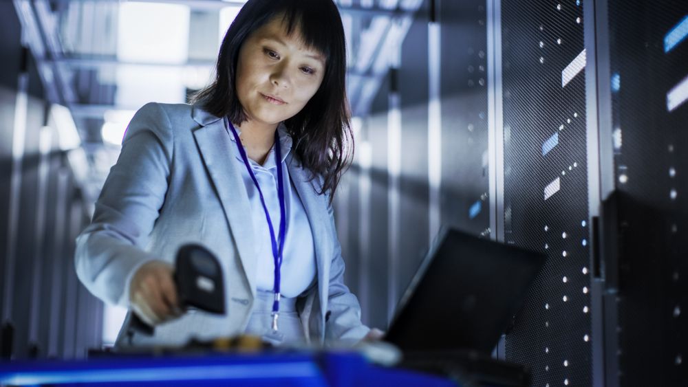 Asian Female IT Engineer Working on a Laptop on Tool Cart, She Scans Hard Drives.