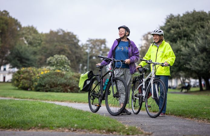 Two happy older people standing and talking with bikes looking away