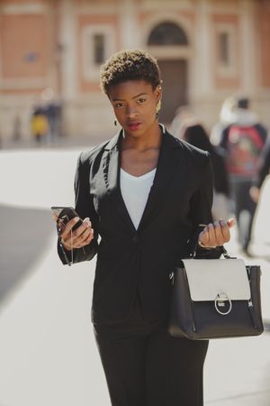 Stylish Black woman with handbag and smartphone on street