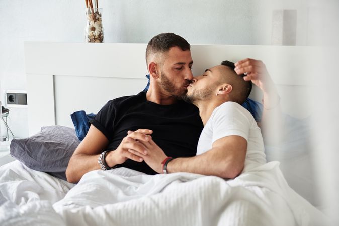 Smiling gay couple hugging and kissing on bed