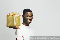 Smiling Black man holding a present wrapped in gold on his shoulder 5RyNA0
