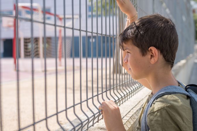 Side view of boy holding fence looking into school yard