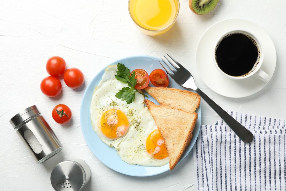Top view of plate of fried eggs for breakfast, with coffee and juice on blue plate