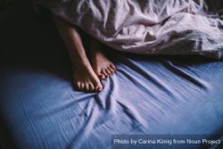 Woman’s feet peaking out from the blankets while lying in bed v4NaZ5
