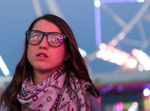 Smiling young woman near illuminated ferris wheel at night