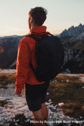 Back view of man in red jacket with backpack standing in the mountains at sunset 0KJGAb