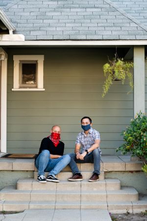 Two men sitting on front porch wearing masks for COVID porch portrait