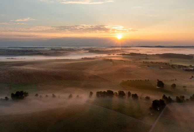 Aerial drone shot of misty agricultural fields and rolling hills at sunrise