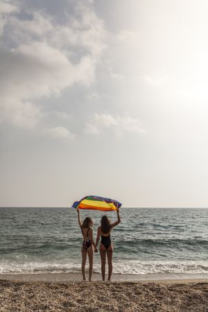 Females standing with rainbow flag on seashore