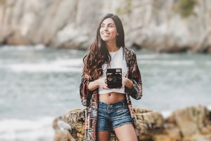 Woman with camera on shore near stones and water