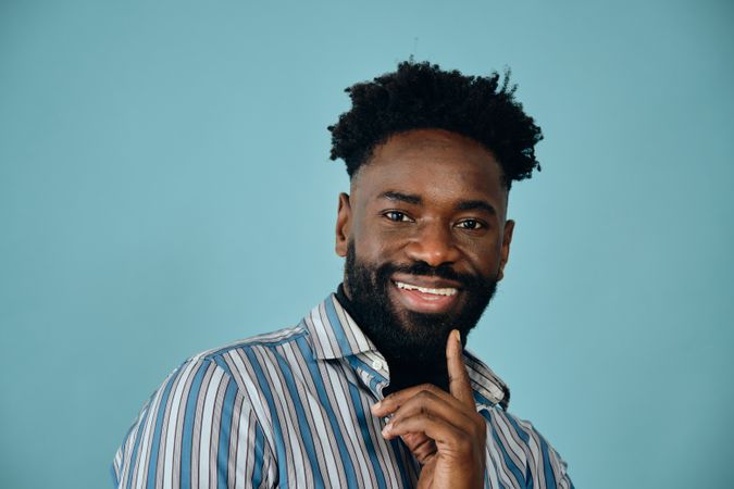 Closeup portrait of a smiling Black man in blue studio shoot with finger to chin