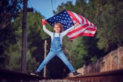 Child with flag of America celebrating Independence Day on railway