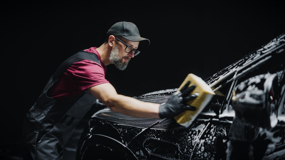 Portrait of a Professional Car Wash Specialist Using a Big Soft Sponge to Wash a High Tech Family Electric SUV with Foam Before Detailing, Polishing and Waxing
