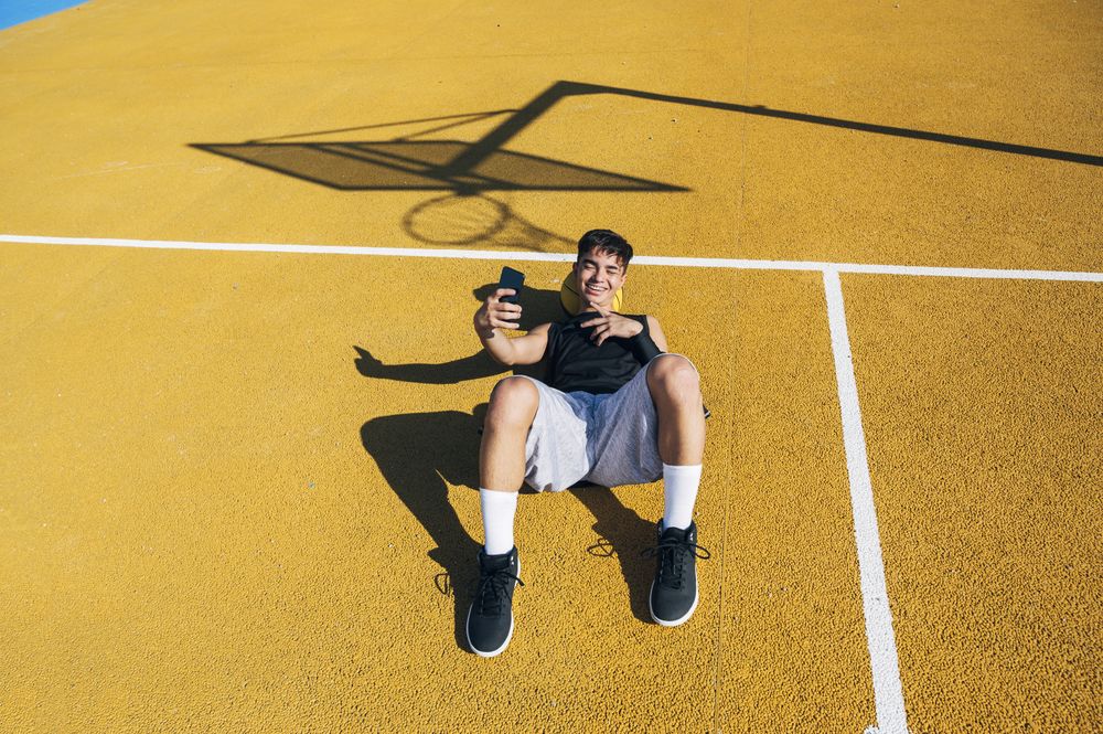 Male basketball player using his smartphone resting after training