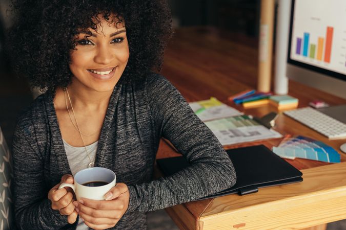 Portrait of happy young woman having coffee at home office desk