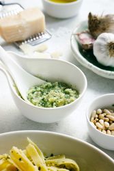Bowl of fresh pesto sauce next to raw ingredients on table