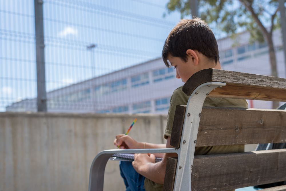 Back of teenage male sitting on bench writing