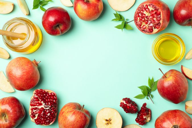 Top view of arrangements of apples, honey, pomegranate on mint green table with copy space