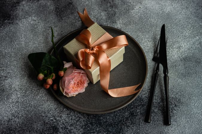 Pink flowers and gift with ribbon on dark plate with grey background