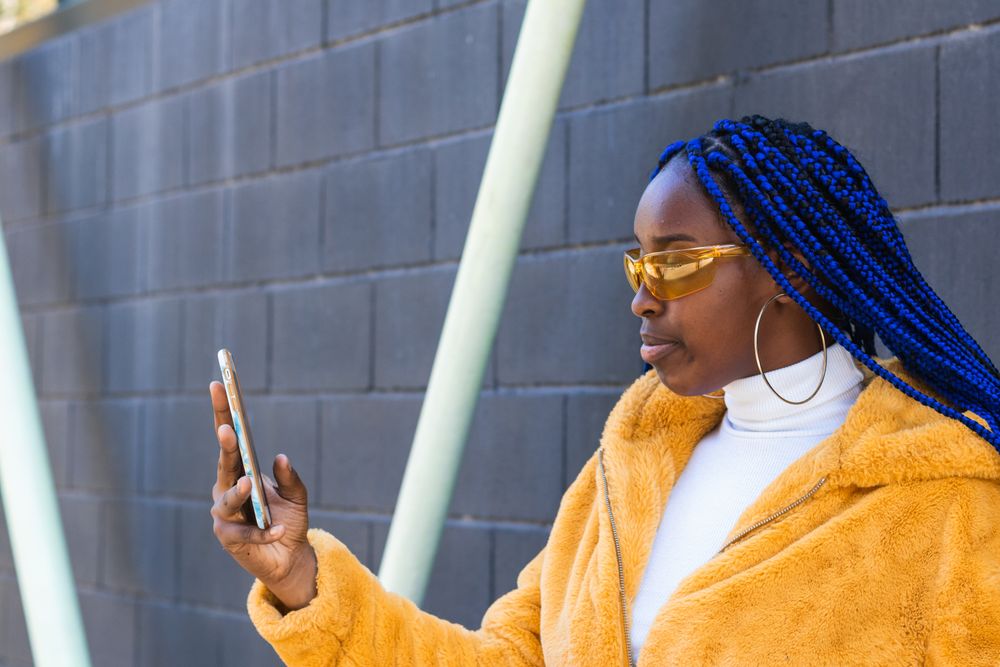 woman in trendy outfit browsing cellphone in city
