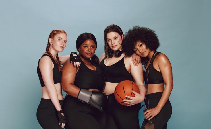 Beautiful group of women with sports equipment looking at camera against grey background