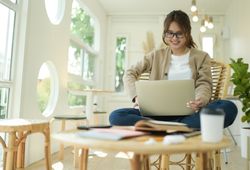 A young woman sits in the living room at home with laptop talking online.
