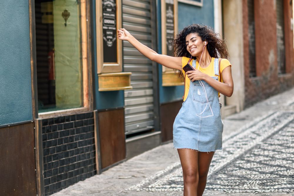 Arab woman listening to music with earphones and dancing in in cobblestone street