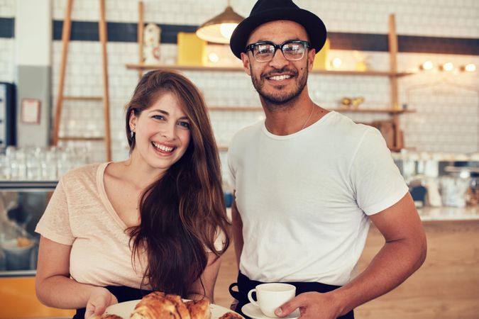 Portrait of happy young man and woman holding their lunch in a cafe looking at camera and smiling