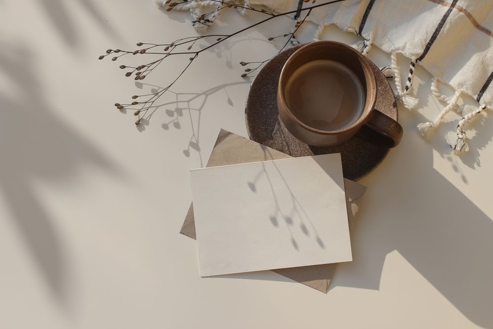 Cup of coffee and checkered plaid on table with blank card and shadow