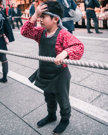 Boy wearing traditional celebration outfit grabbing a rope standing on street in Japan