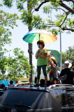 Los Angeles, CA, USA — June 14th, 2020: child standing on roof of car with rainbow umbrella
